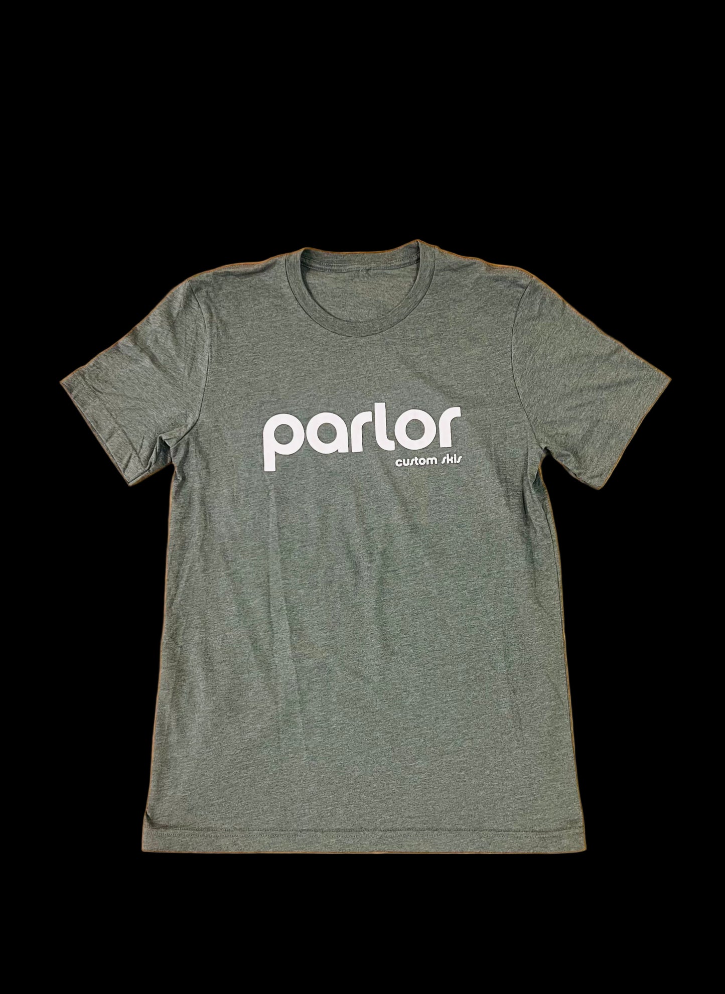 A green t-shirt with the 'PARLOR' brand logo printed in white on the front and back, placed on a wooden surface.