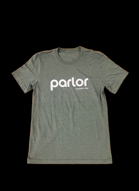 A green t-shirt with the 'PARLOR' brand logo printed in white on the front and back, placed on a wooden surface.
